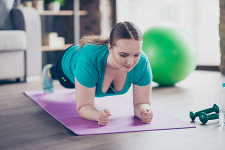 Close up portrait of confident concentrated chubby fatty young cute positive woman standing in plank...