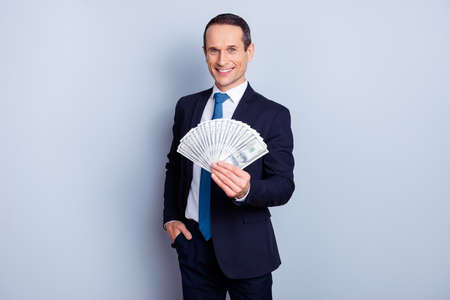 Portrait of glad confident smart businessman demonstrating presenting fan made of dollars in hand isolated on gray backgroundの写真素材