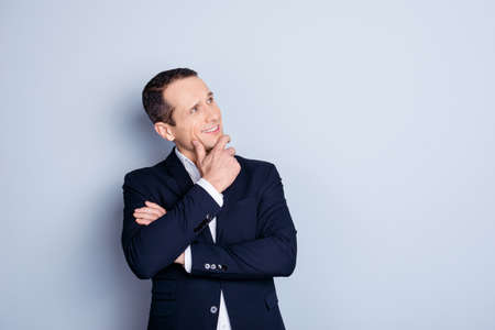 thoughtful man in formal wear holding hand on chin, looking at copy space standing over gray backgroundの写真素材