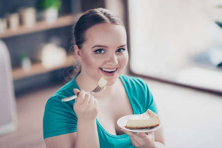 Close up portrait of happy cheerful excited delightful fat sportive curvy chubby excited hungry woman is enjoying cheesecake on a plateの写真素材