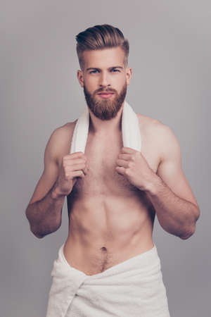 Vertical portrait of handsome neat serious attractive stunning sportive sexy muscular man with modern hairdo white towel on hips holding small towel on neck isolated on gray backgroundの写真素材