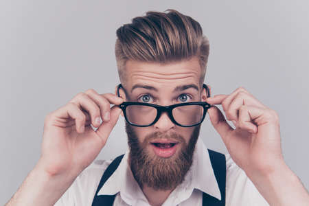 Close up portrait of handsome virile masculine emotion expressing groomed classy smart intelligent clever manager with big eyes touching rimmed glasses isolated on gray backgroundの写真素材