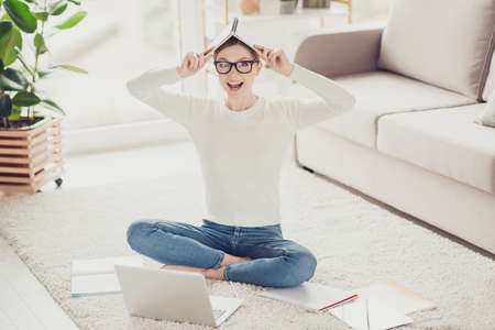 Foolish, attractive, funny, smart girl, sitting with crossed legs on carpet at home holding notebook...