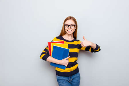 Academic exam copybook people teacher tutor fun joy enjoy concept. Portrait of pretty cheerful joyful rejoicing cute lovely teenager showing thumb-up holding book isolated on gray backgroundの写真素材