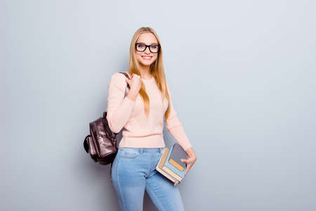 Portrait of clever smart intelligent concentrated focused excited cheerful with toothy beaming smile teen age student carrying backpack on shoulder holding pile of book isolated on gray backgroundの写真素材