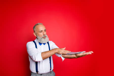 Professional, handsome, trendy, attractive old man with blue bowtie and suspenders spread deck of cards along the arm with one hand over red background, having pout lips, serious concentrated expressionの写真素材