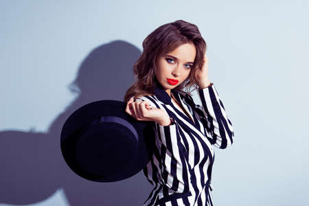 Portrait of chic classy beautiful attractive pretty elegant graceful elite stunning lovely cute tender gentle gorgeous woman with brown curly wavy hair holding hat in hand isolated on ray backgroundの写真素材