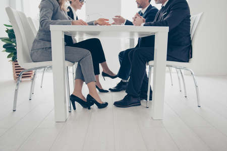 Side view, cropped, bottom view portrait of stylish, attractive, classy business people's legs under table, in suits, sitting in work place, station, having conference, consulting, clients, brokersの写真素材