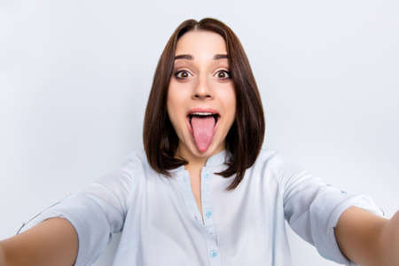Self portrait of pretty, charming, comic, childish, funny girl with modern hairstyle gesture tongue...