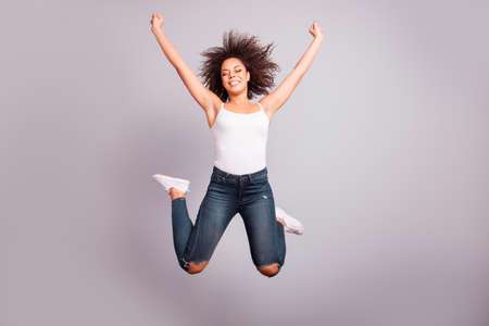 Full size portrait of cheerful, confident, attractive, funny, crazy, funky girl in jeans, sneakers, having fun, leisure, rest, relax, celebrating pass exams with close eyes over grey backgroundの写真素材