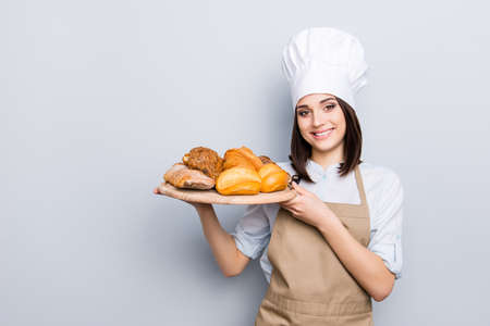 White uniform high hat industry manufacture people eating nutrition concept. Portrait of charming woman carrying wooden round tray full of yummy palatable nourishing bread isolated on gray backgroundの写真素材