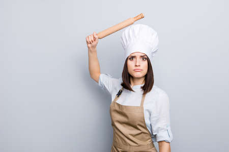 Expel penalty humorous joke bad concept. Portrait of pretty sad upset laughable annoyed irritated chef with raised wooden pin in hand wants to beat you unskilled assistant isolated on gray backgroundの写真素材