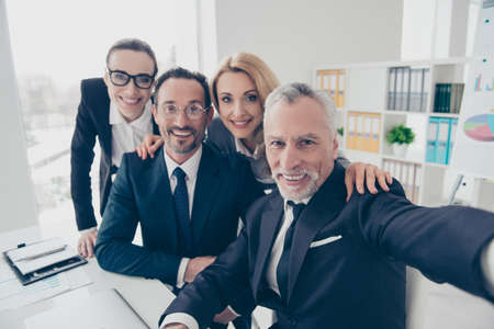 Portrait of four smiling, financial, attractive business people in glasses, spectacles, shooting selfie on front camera, sitting at desktop, gathering in work place, station, having break, rest, relaxの写真素材