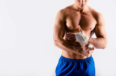 Cropped close up photo of strong sportive nude man in blue shorts, he is bandaging his hands, preparing to fight, isolated on white background, copy spaceの写真素材