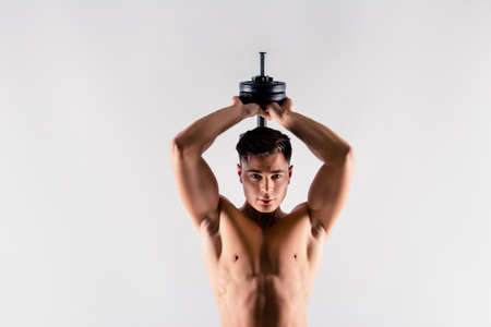 Cropped close up photo of handsome muscular virile strong man lifting a dumbbell from behind his back, he is training his triceps, isolated on grey background, copy-spaceの写真素材