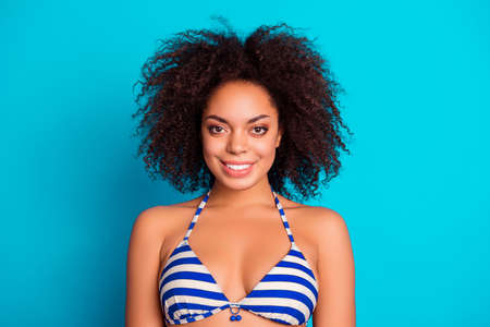 Beaty people leisure lifestyle concept. Close up portrait of happy cute lovely with lush fluffy curly hair bronze tanning afro woman wearing striped top of a swimsuit, isolated on blue backgroundの写真素材