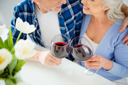 Cropped close up top view portrait with half face of lovely cheerful attractive romantic couple enjoying sitting in the kitchen clinking glasses with red wine looking at each other having funの写真素材