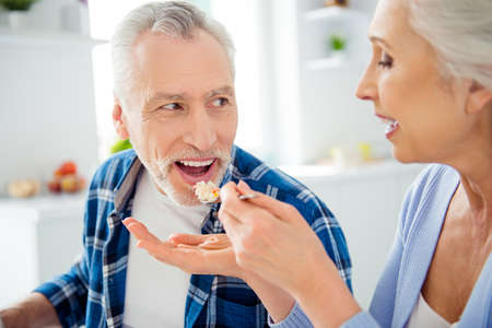 Beautiful woman with wrinkle feeding with fork her handsome lover with bristle, holding meal near...