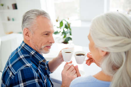 Attractive lovely sweet stylish couple sitting at the table in kitchen drinking coffee, looking at each otherの写真素材