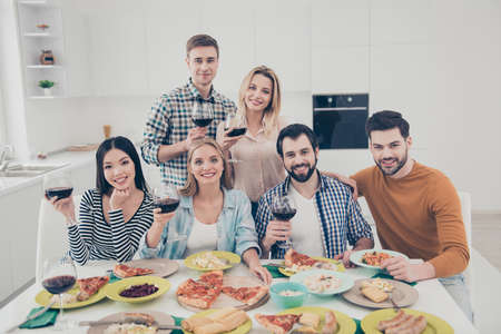 Portrait of stylish, trendy, handsome, beautiful, close, attractive friends holding glasses with red wine in hands sitting at the table having dinner supper celebrating holiday eventの写真素材