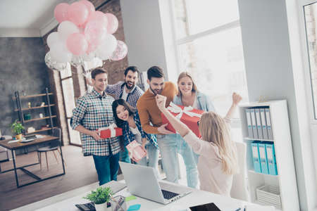 Creative, stylish, attractive, cheerful business people making surprise for their happy colleague, manager with raised hands up who sitting at desk top, having cases in package with bowの写真素材