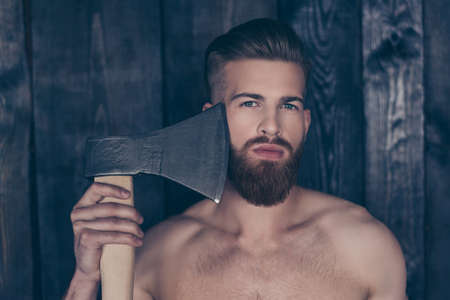 Barber shop barbershop. Close up portrait of sexy handsome naked manly serious concentrated confident attractive stylish logger feller trying to shave beard using axe isolated gray wooden backgroundの写真素材
