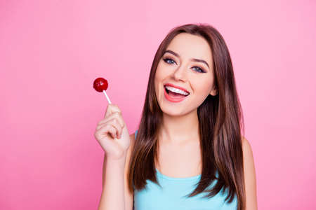 Portrait of cute tender gentle sweet attractive having fun carefree amazing woman wearing blue singlet holding red candy, isolated on vivid pink backgroundの写真素材