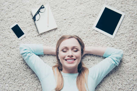 Top high angle view portrait of positive, dreamy, charming, cute, nice, pretty woman holding hands behind head with close eyes imagine trip, travel, having good memories, laying on the floor at homeの写真素材