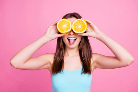 Portrait of amusing comic entertaining humorous laughable beautiful lovely cute pretty joke girl fooling around playing with orange slices, isolated on pink backgroundの写真素材