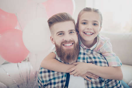Portrait of stylish cheerful positive family with one child, cute toothy daughter embracing her trendy father in piggy back style having air ballons looking at camera wearing casual outfitsの写真素材