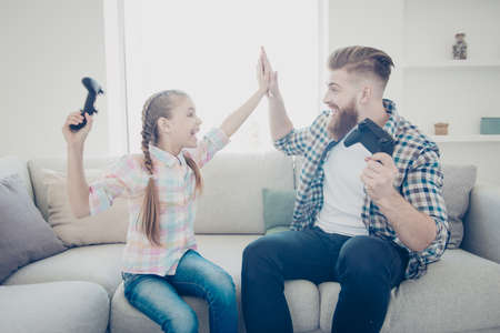 Good job my best friend! Cheerful joyful positive stylish family with one parent, dad giving high five to daughter after victory in car racing game on x-box sitting in modern house screaming yellingの写真素材