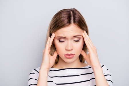 Portrait of sad, upset, unhappy, pretty, charming, stylish girl in striped outfit touching temples with fingers having close eyes suffering from headache isolated on grey backgroundの写真素材