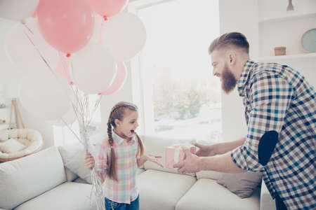 Bearded father giving gift case in pink package with white bow to excited shocked surprised wondered amazed daughter holding air balloons dreams come true standing in house modern apartmentの写真素材