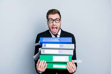 I have no time to fill in all the documents! Portrait of frustrated perplexed frightened shouting office worker holding pile of folders in hands, isolated on gray background, copy-spaceの写真素材