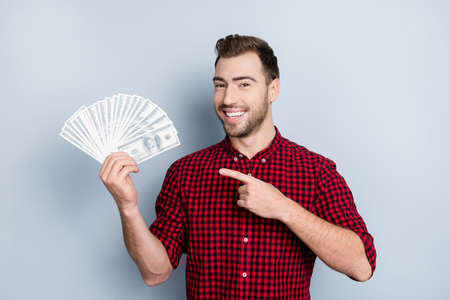 Portrait of handsome confident with toothy beaming smile smart rich wealthy friendly cheerful excited entrepreneur demonstrating many banknotes in hand with forefinger isolated on gray backgroundの写真素材