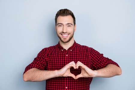 My heart belongs to you! Portrait of excited in love sensual tender gentle cute with toothy smile guy wearing red checkered shirt imitating heart using his hands, isolated on gray backgroundの写真素材