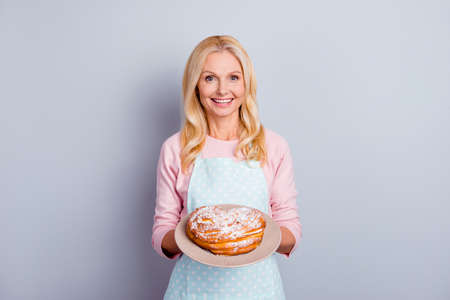Portrait of pretty charming cheerful aged woman with wrinkle showing gesturing sweet homemade pie tasty bun isolated on grey background, specialty of the houseの写真素材