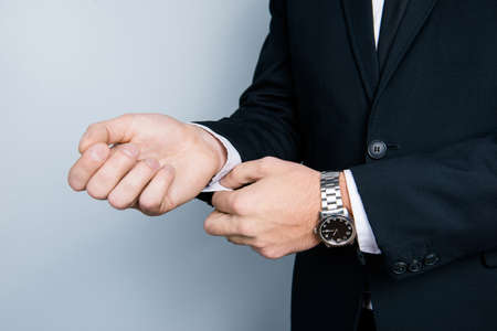 Cropped close up photo of businessman's hands correcting cufflincs on white shirt, wearing black...