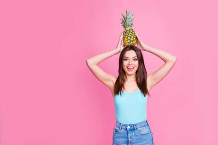 Look what I can do! Portrait of cute laughing cheerful crazy excited adorable lovely playful funky fancy attractive girl holding a pineapple on head having fun, isolated on pink backgroundの写真素材