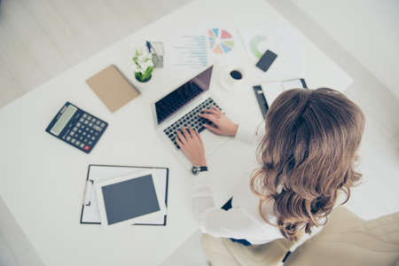 Top view portrait of woman with curls, hairdo holding hands on keyboard making presentation, project, report, having accessories on her desk sitting on armchair using wi-fi internetの写真素材