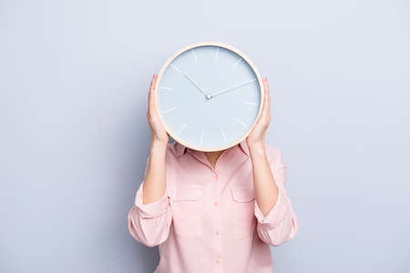 It's 10:10 o'clock. Portrait of charming pretty positive cheerful woman closing covering head face with round clock isolated on grey backgroundの写真素材