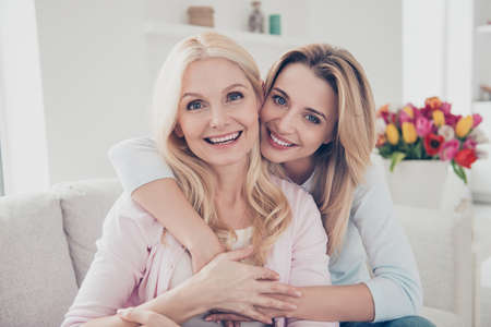 Portrait of pretty charming cheerful trendy positive mother and daughter sitting on couch in living...