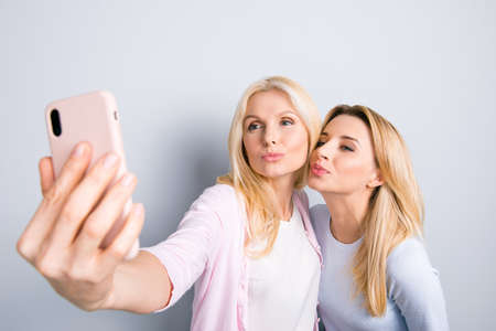 Funky happy cute lovely mother and daughter shooting self portrait on front camera of smart phone...