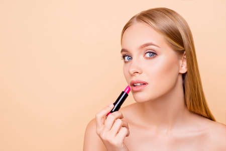 Portrait with copy space, empty place for advertisement of cute charming girl with soft smooth perfect skin testing pink lipstick looking at camera isolated on beige background, wellbeing conceptの写真素材