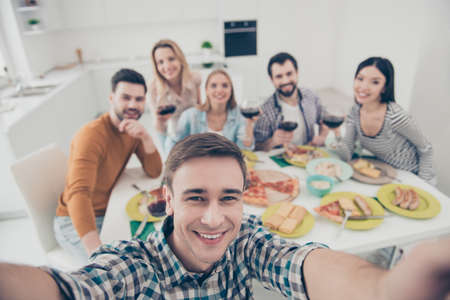 Handsome, attractive, stylish man making self portrait with best friends on blurred background sitting at the table holding glasses with red wine, celebrating holiday indoorの写真素材
