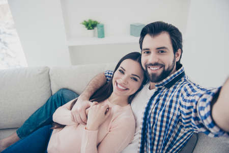 Self portrait of cheerful positive  couple with beaming smiles lying indoor in house, shooting selfie on front camera. True feelings lovestory conceptの写真素材