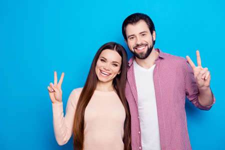 Portrait of joyful attractive couple, bearded guy and brunette girl with long hair gesturing v-signs...