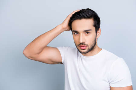 Portrait of manly stunning man in white outfit touching fixing correcting his perfect smooth healthy hair looking at camera isolated on grey background, hair therapy trouble conceptの写真素材