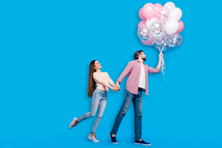 Full size body portrait of funny comic partners in jeans sneakers casual outfits having many air balloons isolated on blue background. Love story conceptの写真素材