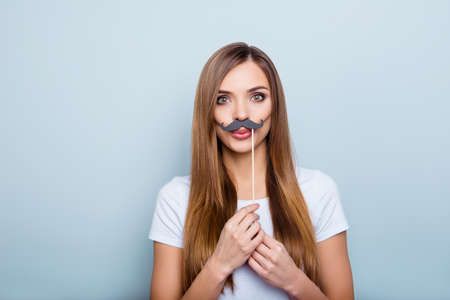 Portrait of creative comic girl holding black carton mustache on stick with pout lips sending kiss looking at camera isolated on grey backgroundの写真素材